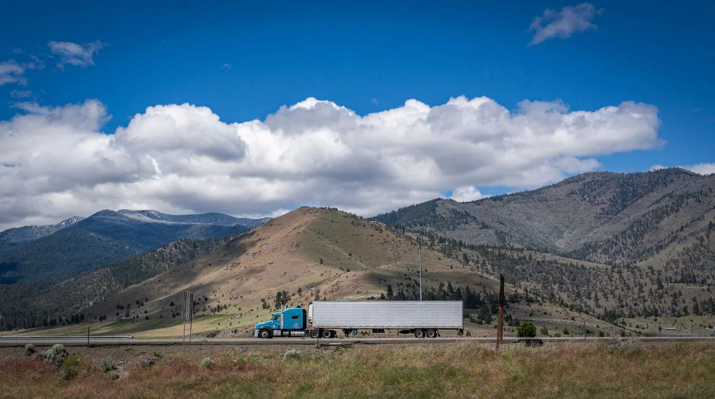 Blue American semi-truck traveling on a highway with mountains in the distance